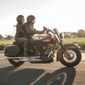 Ein Paar in Motorradbekleidung fährt auf einer Harley-Davidson bei Sonnenuntergang über eine Landstraße.