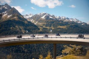 Motorradfahrer fahren auf einer kurvenreichen Straße mit beeindruckender Berglandschaft im Hintergrund.