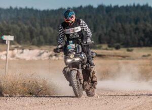 Ein Motorradfahrer in Schutzkleidung fährt auf einem unbefestigten Weg mit einer Harley-Davidson durch die Natur.