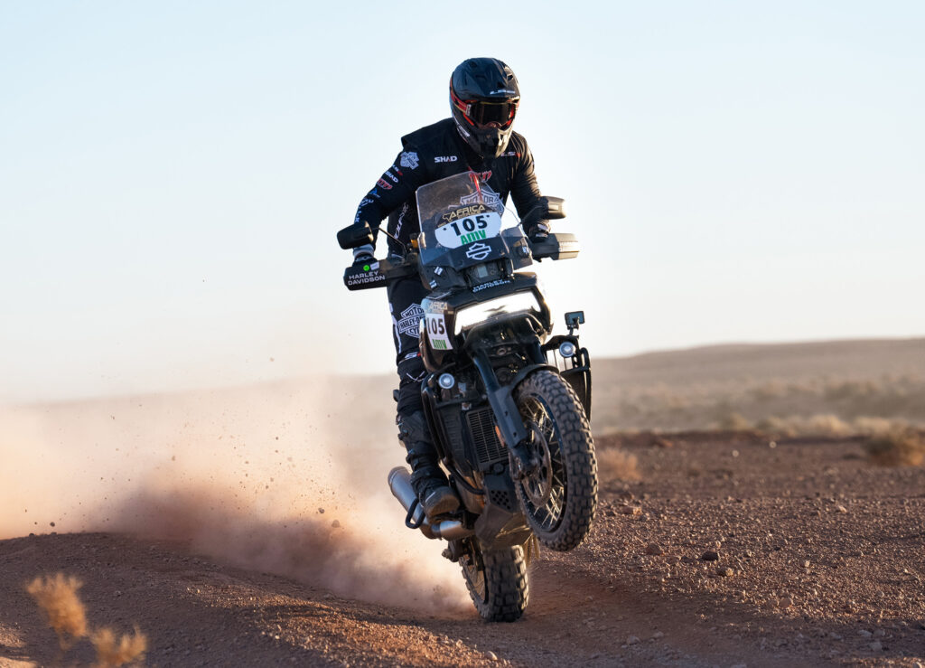 Motorradfahrer auf einer Harley-Davidson hebt das Vorderrad auf einem staubigen Gelände an.