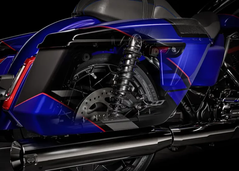Detailaufnahme eines blauen Harley-Davidson-Motorrads, die den Hinterreifen, die Federung und den Auspuff zeigt.