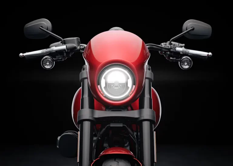 Frontansicht eines roten Harley-Davidson Motorrads mit beleuchtetem Scheinwerfer auf schwarzem Hintergrund.