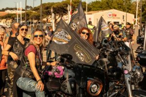Verschiedene Motorradfahrerinnen und Motorradfahrer feiern zusammen mit Harley-Davidson Flaggen und Motorrädern auf einem Festival.