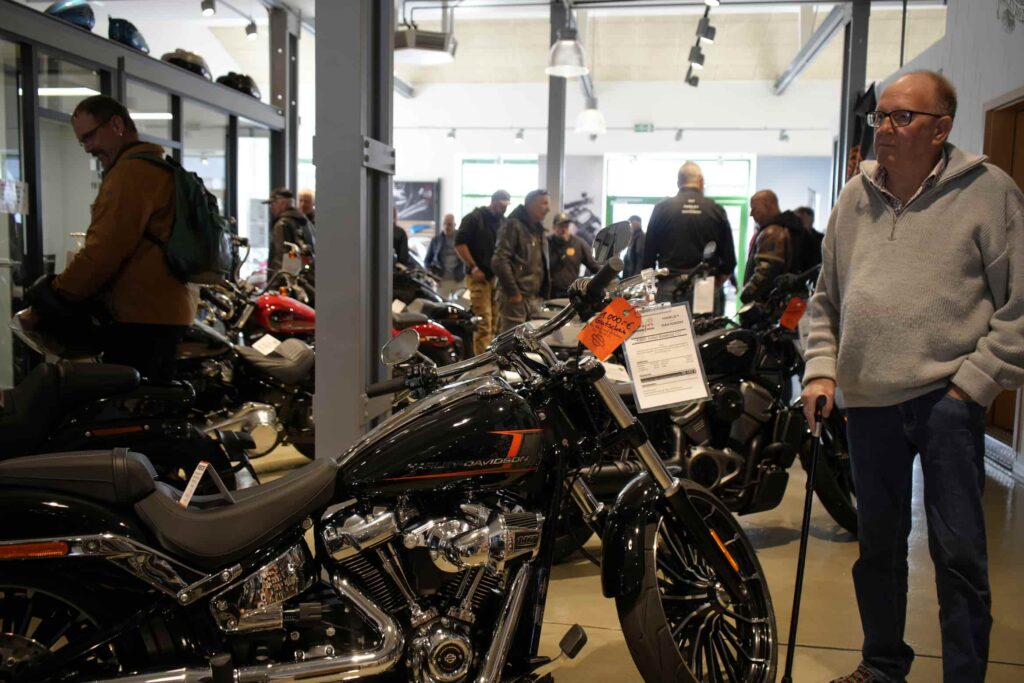 Ein Kunde betrachtet eine Harley-Davidson-Motorrad in einem modernen Verkaufsraum, umgeben von weiteren Motorrädern und interessierten Besuchern.
