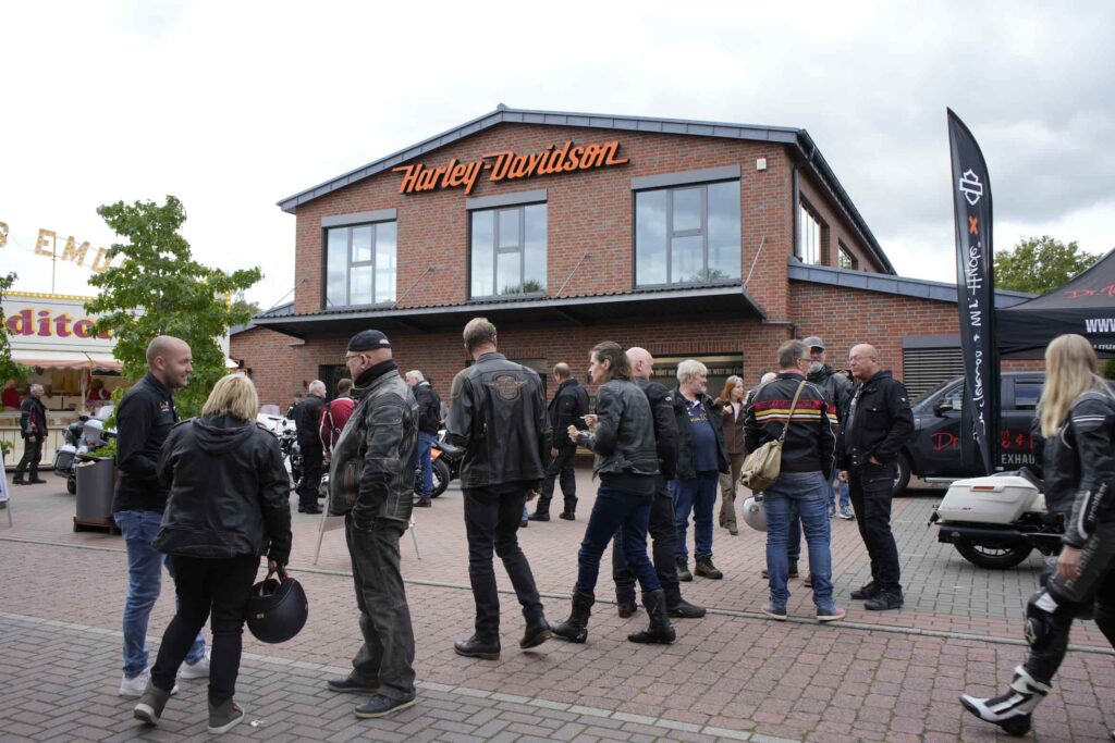 Menschen in Motorradbekleidung stehen vor dem Harley-Davidson Händler Börjes American Bikes, umgeben von Motorrädern und einem Festzelt.