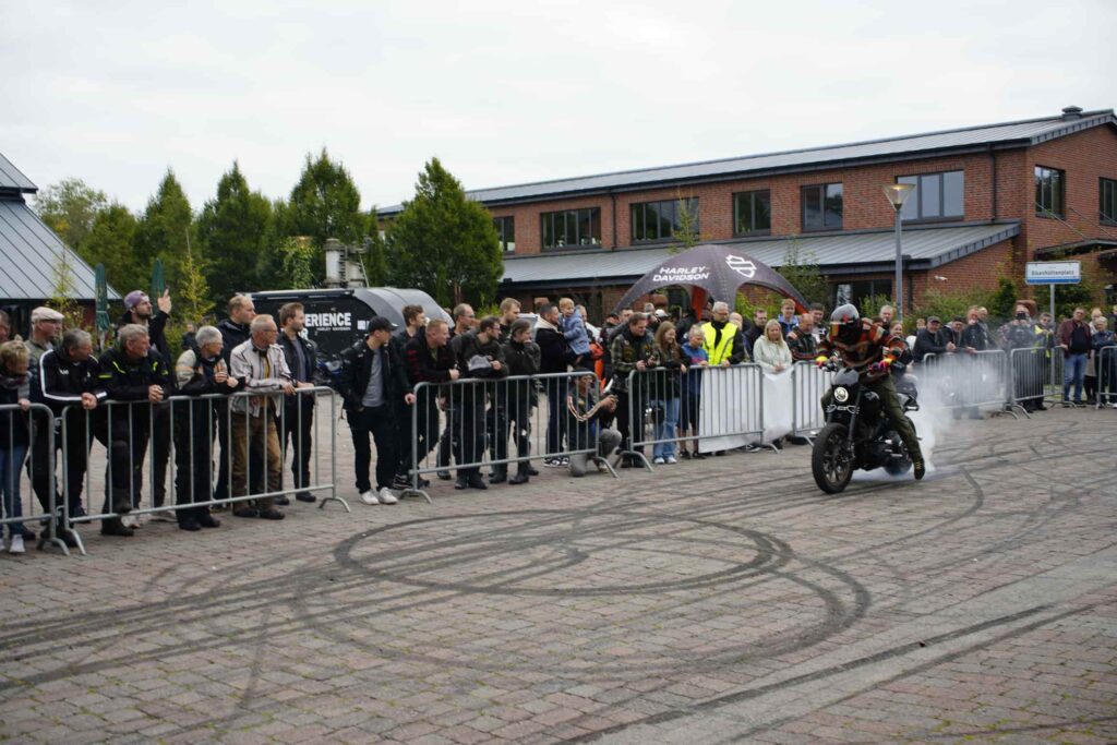 Eine Gruppe von Motorrad-Enthusiasten beobachtet einen Stuntfahrer, der mit einer Harley-Davidson auf einem Event in Augustfehn rauchende Reifen hinterlässt.