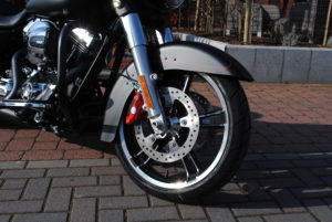 Nahaufnahme des Vorderrads einer Harley-Davidson mit glänzenden Chromteilen und sportlichem Design auf einem gepflasterten Untergrund.