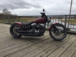Eine stilvolle Harley-Davidson-Motorrad in glänzendem Rot steht auf einer Holzplattform mit Blick auf einen ruhigen Wasserlauf.