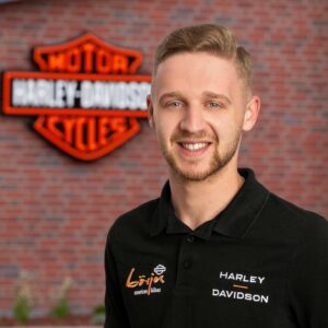 Portrait eines freundlichen Mitarbeiters von Börjes American Bikes vor dem markanten Harley-Davidson-Schild.