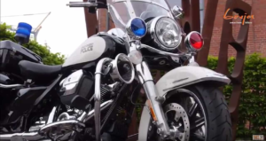 Eine Harley-Davidson Polizei-Motorrad mit blauen und roten Lichtern steht vor einer grünen Hecke.
