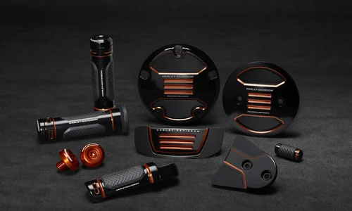 Verschiedene Harley-Davidson Motorradteile und Zubehör in Schwarz mit orangefarbenen Akzenten auf dunklem Hintergrund.